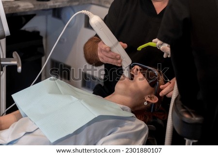 Orthodontist using a digital scanner to digitally capture the shape of teenager girl patient teeth and gums for custom made invisible plastic aligners bracers.