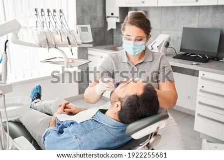 The orthodontist wearing protective mask demonstrates to the male patient the impression tray in which the silicone impression material will be placed to get the shape of his teeth