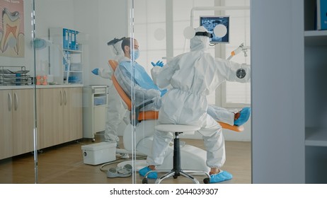 Orthodontists And Patient Wearing Ppe Suits In Oral Cabinet For Teeth Examination During Pandemic. Dentist And Assistant Using Dental Equipment And Tools For Professional Consultation