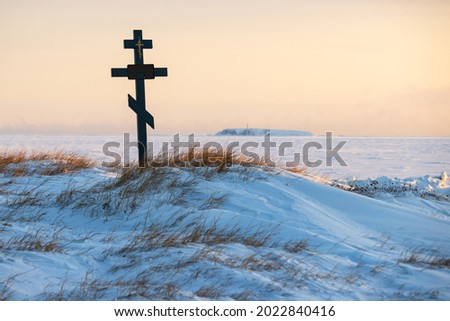 Orthodox cross in the snowy tundra on the coast of the frozen sea. An old cemetery in the far North of Russia in the Arctic. Snow-covered grave. Chukotka, Polar Siberia, Russia. Cold winter weather.