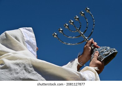 Orthodox Jewish man holding a temple Menorah against clear blue sky. - Shutterstock ID 2081127877