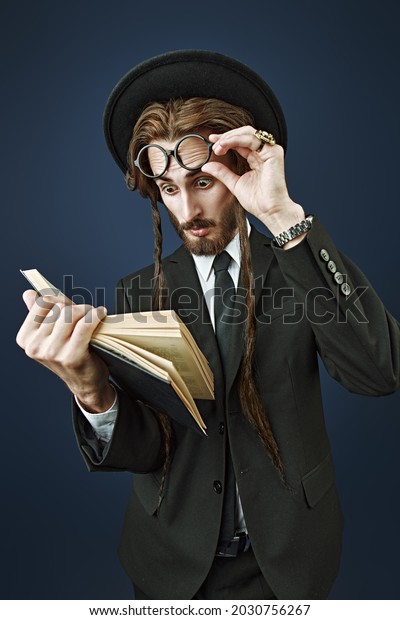 An Orthodox Jewish man reads the Torah.\
Studio shot on a dark blue background.\

