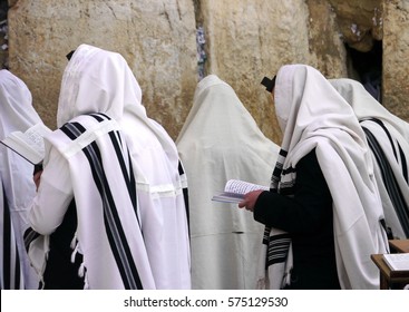 Orthodox Jews wearing tallit shawls are praying with Siddur prayer books at the Western/Wailing Wall or Kotel, holiest site in Judaism; Jerusalem Israel