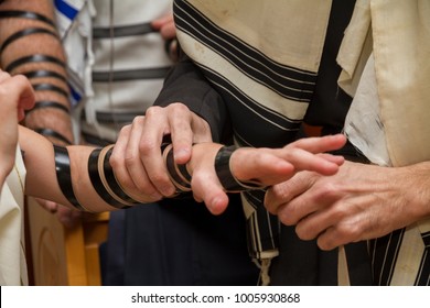 An orthodox man, wearing prayer shawl, put a Jewish Tefillin on A young man arm preparing for a pray, as part of a Jewish ritual, Bar Mitzvah ceremony