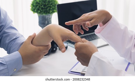 Orthopaedic Doctor Doing Physical Examination Patient With Wrist Pain At The Clinic. Physical Therapist Checks The Patient Wrist By Pressing The Wrist Bone.