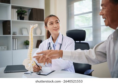 Orthopedic doctor educating aging patient about spinal health and posture using a human spine model.
