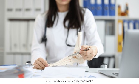 Orthopedic doctor explains physiology of bone model by pointing to point of model. Tell patient how to treat bone disease - Shutterstock ID 2395305607