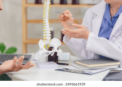 An orthopedic doctor shows a spinal model to a patient in a human spinal hospital. Diseases and disorders of the spinal cord, back pain, lumbar pain, orthopedic surgery, chiropractic, office syndrome