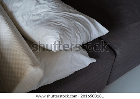 Orthopedic memory foam and regular white pillows stacked on a dark sofa