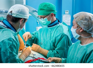 Orthopedic Surgeons In Sterile Uniform And Gloves Working As A Team In The Operating Room, Performing Real Surgery On A Patients Spine. 