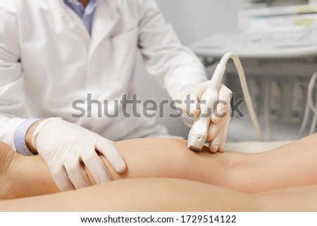 Orthopedist doctor doing ultrasound examination of patient's leg veins in his office. Young woman passing ultrasound scan in clinic. Doctor work. Medical research.