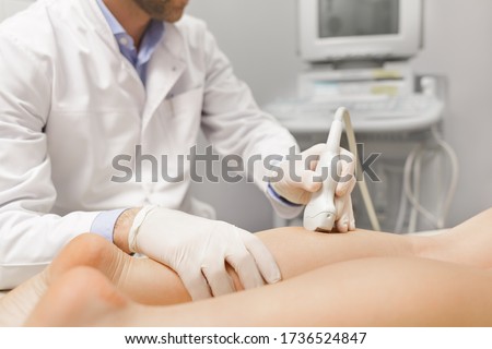 Orthopedist doctor doing ultrasound examination of patient's leg veins in his office. Young woman passing ultrasound scan in clinic. Doctor work. Medical research.
