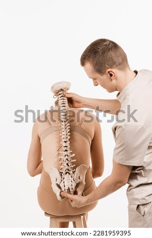 Orthopedist showing spinal column model with girl on white background. Scoliosis is sideways curvature of the spine. Backbone anatomical model with young woman