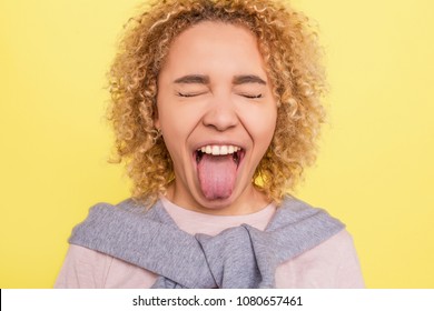 ortrait of a girl that has closed her eyes and showing her tounge outside of the mouth. She is very funny. Isolated on yellow bachground
