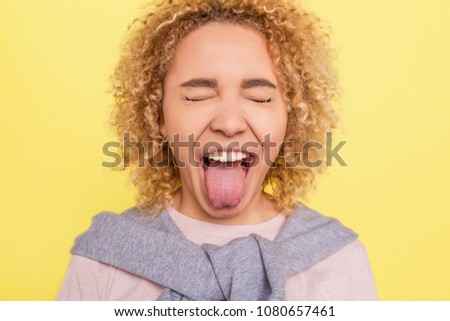 ortrait of a girl that has closed her eyes and showing her tounge outside of the mouth. She is very funny. Isolated on yellow bachground