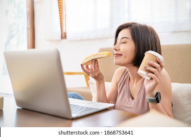 Ortrait Of Happy Asian Woman Working On Laptop Computer, Have Lunch Break Eating Pizza In Sofa Living Room Using Internet. Delivery, Work From Home Quarantine New Normal With Copy Space Background