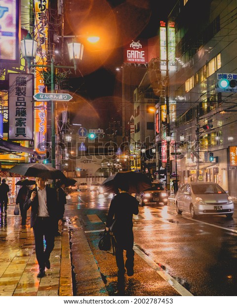 Osaka, Japan - Circa 2015: Restaurants, stores,\
people in bikes and walking, cars and traffic, lights, neons and\
signs in a rainy night with reflections in the floor at Nipponbashi\
in the night