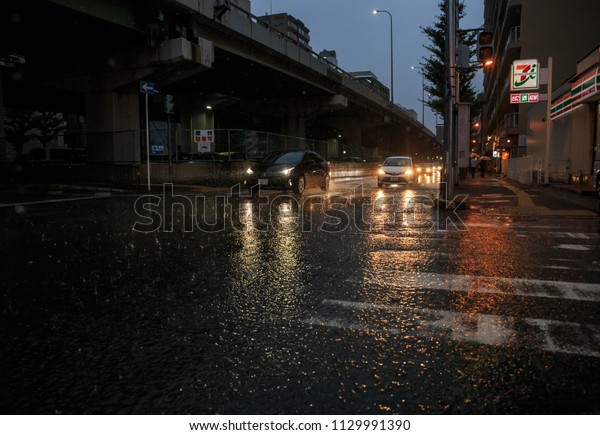 Osaka, Japan - July 5, 2018: Car\
headlights reflect off flooded street during heavy rain storm which\
caused damage and flooding throughout southern\
Japan