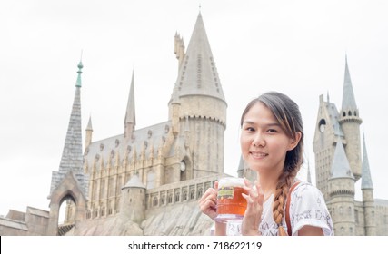 Osaka, Japan - SEPTEMBER 19, 2016 : asian visitor smile pose take a shot with butterbeer in front of hogwarts castle in wizarding world of harry potter in universal studio theme park in osaka japan.