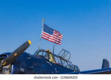 OSHKOSH, UNITED STATES - Jul 25, 2021: An American flag flying over a blue world war 2 vintage warbird airplane