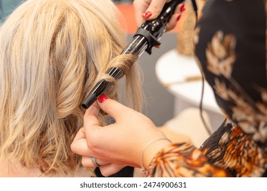 Osijek Croatia - 7 06 2024: Health and Beauty Fair. close-up shot of a woman getting her hair curled with a curling iron at a hair salon. The stylist is holding the curling iron  - Powered by Shutterstock