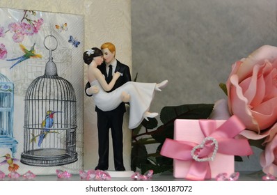 Oslo, Norway -05-10-2014: Wedding Decorations In A Display Window. Funny Wedding Cake Topper. Swept Up In His Arms Wedding Couple