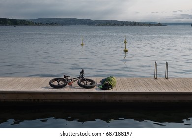 Oslo, Norway - 20 May 2017 - Man Lying Down Beside His Fat Bike On Wood Jetty In The Oslo Fjord On Sunny Summer Day