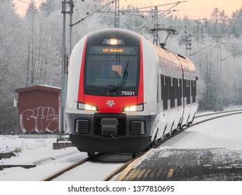 Oslo, Norway - December 24, 2018: Stadler FLIRT regional trains operated by Norwegian State Railways arriving at Sonsveien Station, south of Oslo, with a frozen winter landscape in the background. 