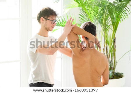Osteopath doing a shoulder evaluation on a man flexing and rotating the joint to assess mobility