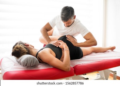 Osteopath performing a liliosacral wing trust treatment on a young woman patient in his clinic in an alternative medicine and healthcare concept