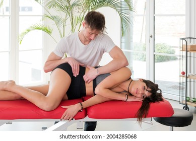 Osteopath performing a sacroiliac myofascial massage on a young woman manipulating the muscles of her sacrum, pelvis ans spine with his hands in a healthcare concept