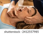 An osteopath performs a jaw adjustment on a female patient, focusing on alleviating tension and improving joint function.