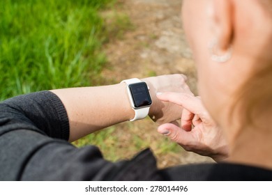 OSTFILDERN, GERMANY - APRIL 26, 2015: A Middle Aged Caucasian Woman Is Checking Her Apple Watch Displaying The Home Screen With A Reminder Of A Current Meeting In Her Calendar While Walking On A Path