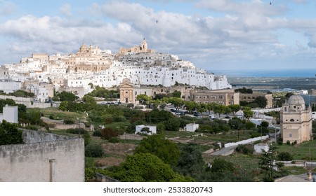 Ostuni Nestled atop a hill, the picturesque town of Puglia is celebrated for its whitewashed buildings, ancient architecture, and vibrant greenery, creating a scenic marvel under a partly cloudy sky. - Powered by Shutterstock