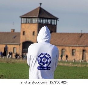 Oswiecim, Poland - March 30, 2016: A High School Student Wearing A Sweater With The Symbol Of The State Trip To Poland As Part Of The Holocaust Study. In The Background Is The Auschwitz Guard Tower