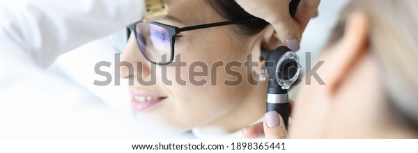 Otolaryngologist doctor examining\
patients ear with otoscope in clinic. Diagnosis of otitis media\
concept