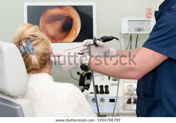 Otolaryngologist doing otitus examination,\
video otoscopy procedure. Hearing clinic. ENT doctor with tools\
wearing mask and gloves examines the patient\'s\
ear.