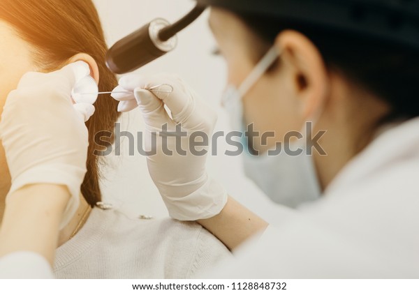 Otolaryngologist\
treats an ear of patient disease and conducts manipulations\
examining the patient\'s ear. Hands in gloves, on the head sterile\
mask and doctor\'s medical\
flashlight