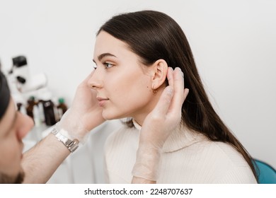 Otoplasty is surgical reshaping of the pinna, or outer ear for correcting an irregularity and improving appearance. Surgeon doctor examines girl ear before otoplasty cosmetic surgery - Shutterstock ID 2248707637