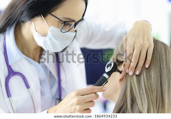 Otorhinolaryngologist looking at patients ear\
with otoscope in clinic. Diagnosis and treatment of otitis media in\
adults\
concept