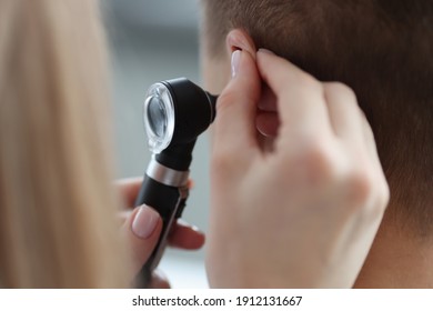 Otorhinolaryngologist pulling ear with his hand and looking at it with otoscope closeup. Otoscopy concept - Powered by Shutterstock