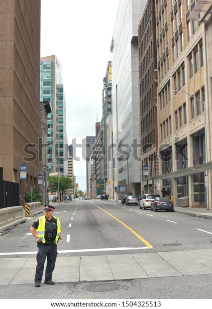 Ottawa, ON - Canada - August 18, 2019 : Police\
Officer standing at the corner of an empty street with no traffic.\
No cars and no pedestrians on the downtown Ottawa Road in\
Canada.