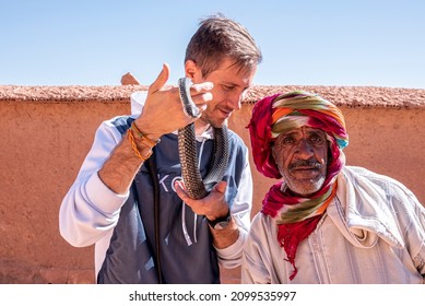 Ouarzazate, Morocco. October 10, 2021. Portrait Of Snake Charmer With Male Tourist Holding Snake