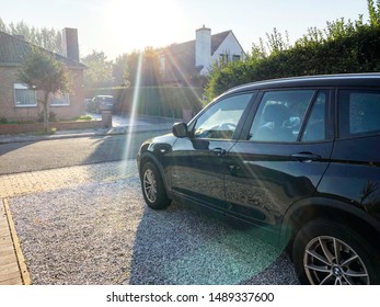 Oudenburg, Belgium - 27 August 2019: Black Car Parked In Driveway Of European House With The Sun Rays Shining Down