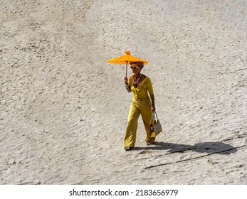 Ouistreham, France September 2021. A Woman Dressed In An Elegant Yellow Style With An Umbrella And Sunglasses Walks Across The Beach Photo From Above