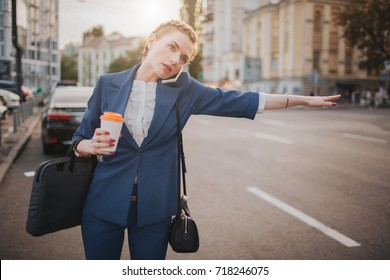 oung stylish businesswoman with coffee cup catching a taxi. Woman doing multiple tasks. Multitasking business woman.
