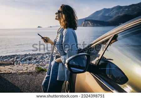 oung woman traveler in a hat standing by her car during summer sea holiday