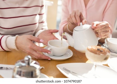 Our breakfast. Young caring girl pouring tea while having lunch with her granny in a cafe - Powered by Shutterstock