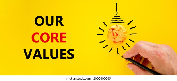 Our Core Values Symbol. Businessman Writing Words 'Our Core Values', Isolated On Beautiful Yellow Background. Light Bulb Icon. Business And Our Core Values Concept. Copy Space.