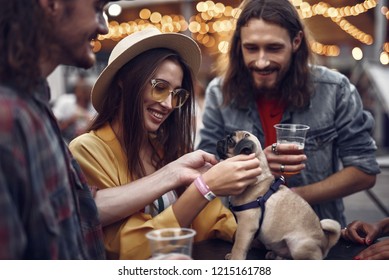 Our Four-legged Friend. Portrait Of Stylish Hipster Friends Looking At Cute Dog And Smiling. Bearded Guy Holding Beer